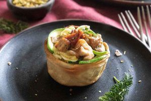 A tartlet filled with the recipe for Mushroom Tulips and raw courgette, presented on a black plate and adorned with some herbs. This delicious and appetising recipe is perfect to surprise your family, friends or your ex.
