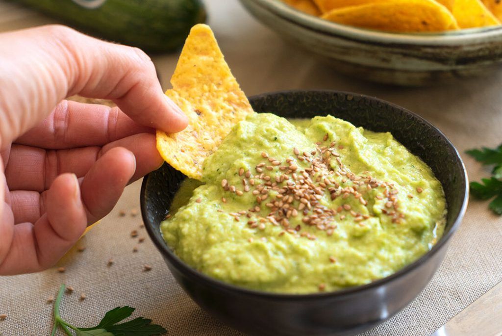Un paté de calabacín crudo que a la vista parece un guacamole, por su color verde y porque está presentado en un bol oscuro y pequeño, redondo, con un Dorito tomando un poco. Tiene unas semillas por encima a modo de decoración. ¡Verde que te quiero verde y si es guacamole de calabacín crudo, más! ¡Apunta esta receta fitness!