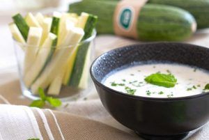 A bowl with tzatziki sauce and a glass with fresh courgette strips as a snack. An easy and delicious recipe that combines the creaminess of the homemade tzatziki sauce with the crunchy texture of the courgette strips.