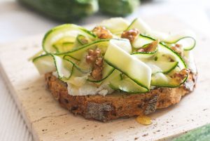 Image of the recipe "Bruschetta with Walnuts," showing a whole wheat toast spread with cheese and garnished with thin slices of zucchini. Chopped walnuts are placed on top of the zucchini, adding a touch of flavor and texture to the dish.