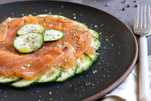 A dish of salmon carpaccio and raw courgette, with the courgette cut into thin slices and the smoked salmon on top. Adorned with olive oil, aromatic herbs, salt and pepper. A quick and elegant recipe that will make you look like a chef.
