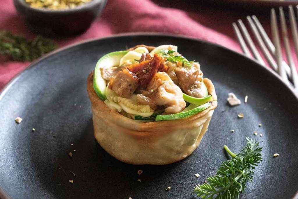 Una tartaleta farcida amb la recepta de Tulipes de bolets i carbassa crua, presentada en un plat negre i adornada amb algunes herbes. Aquesta recepta deliciosa i apetitosa és perfecta per sorprendre la teva famÃlia, amics o el teu ex.