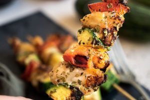Image of the "Zucchini Cru Brochette" recipe, showing a clear picture of a raised brochette, with three blurred brochettes in the background. This recipe is perfect for conquering any heart.